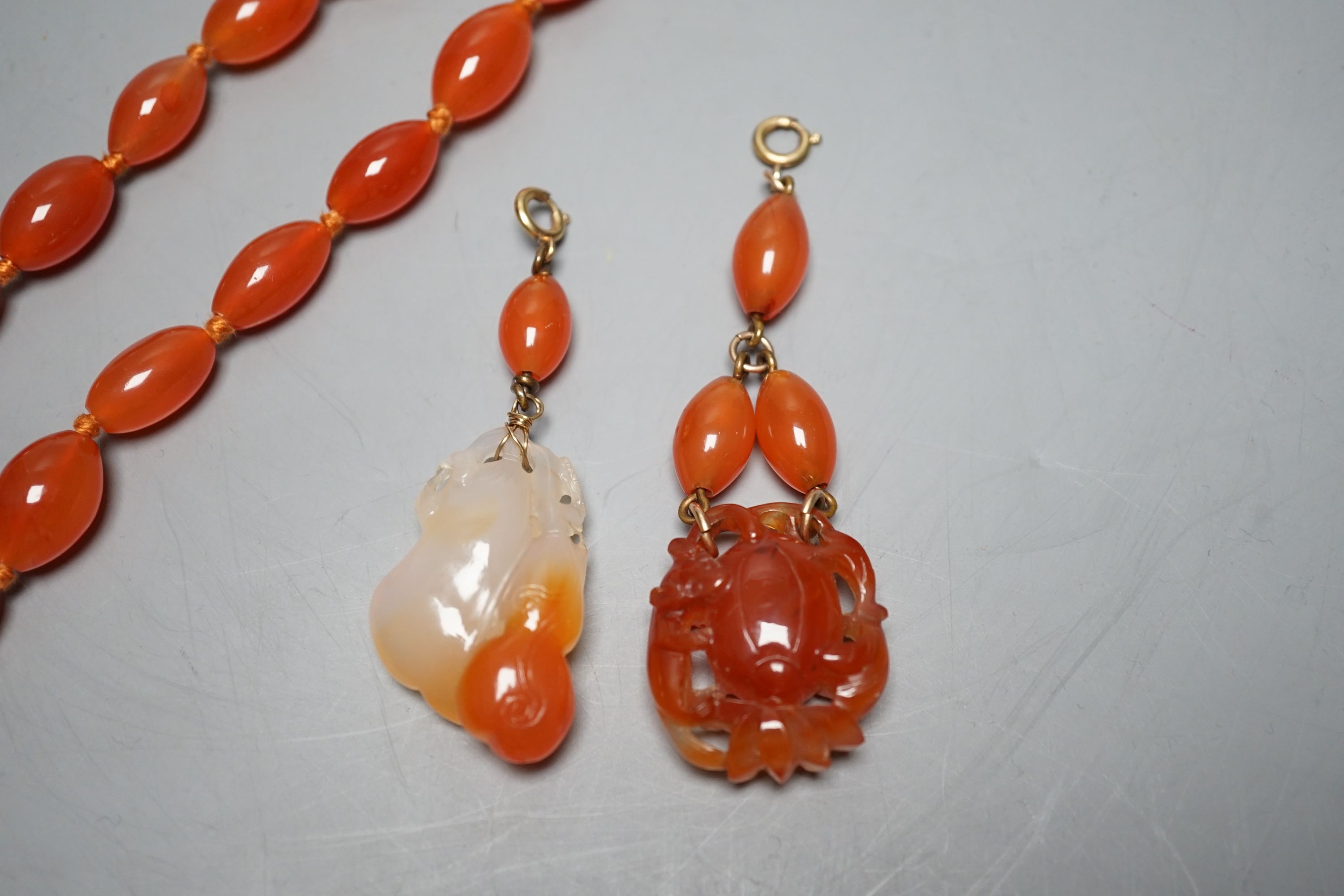 Two carved agate and carnelian bead pendants and a carnelian bead necklace, 48cm.